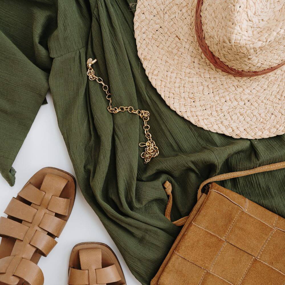 Flache Aufsicht auf Mode-Accessoires wie Strohhut, Ledertasche, Sandalen und Schmuck